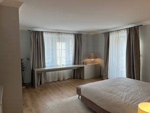 A bedroom with a bed, a bedside table, a lamp, a desk, and curtains.