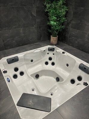 Een bubbelbad met meerdere jets, een bedieningspaneel en een kleine plant in de hoek.