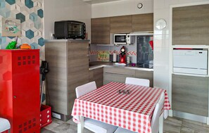 A compact kitchen with a microwave, toaster, and refrigerator. There's a red cabinet with a phone and a small table with a checkered tablecloth. - Bel app. en première ligne (Biscarrosse)