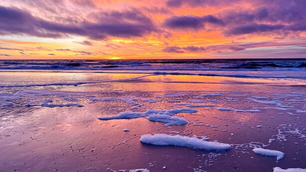 Een strand met golven en een zonsondergang.
