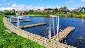 Een kanaal met een sluis, een grasrijke oever en huizen op de achtergrond.