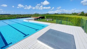 Een zwembad met helderblauw water, omringd door een betegeld zonnedek en een gazon.