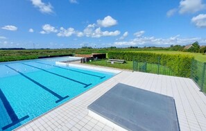 Ein Swimmingpool mit klarem, blauem Wasser, umgeben von einer gefliesten Terrasse und einer Rasenfläche.