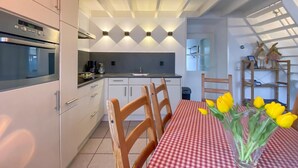 Een moderne keuken met inbouwapparatuur, een eethoek met geruit tafelkleed en een vaas met gele tulpen.