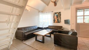 Een woonkamer met een zithoek, een salontafel, een televisie en een hertenhoofd aan de muur.