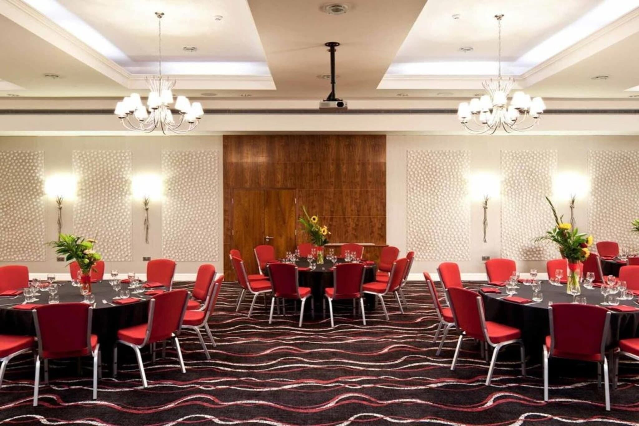 A conference room with round tables, red chairs, chandeliers, and patterned walls.