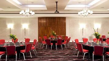 A conference room with round tables, red chairs, chandeliers, and patterned walls.