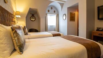 A hotel room with two beds, a wooden headboard, a mirror, a wall-mounted TV, and a door leading to another room.