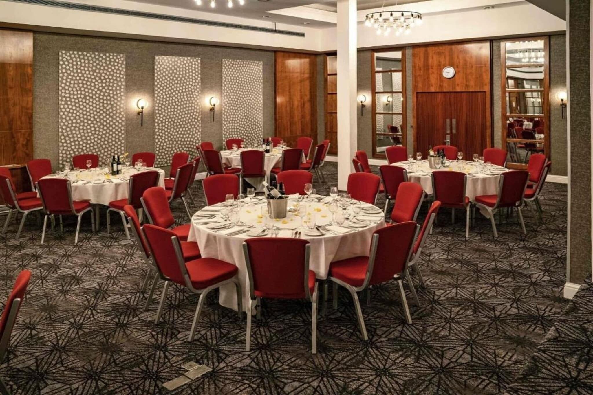 A conference room with round tables, red chairs, and a patterned carpet.