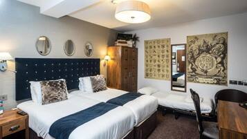 A hotel room with two beds, a desk, a chair, a wardrobe, and decorative wall art.