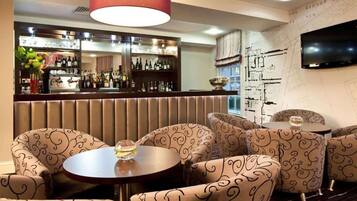 A bar area with a mirrored wall, patterned chairs, and a television mounted on the wall.