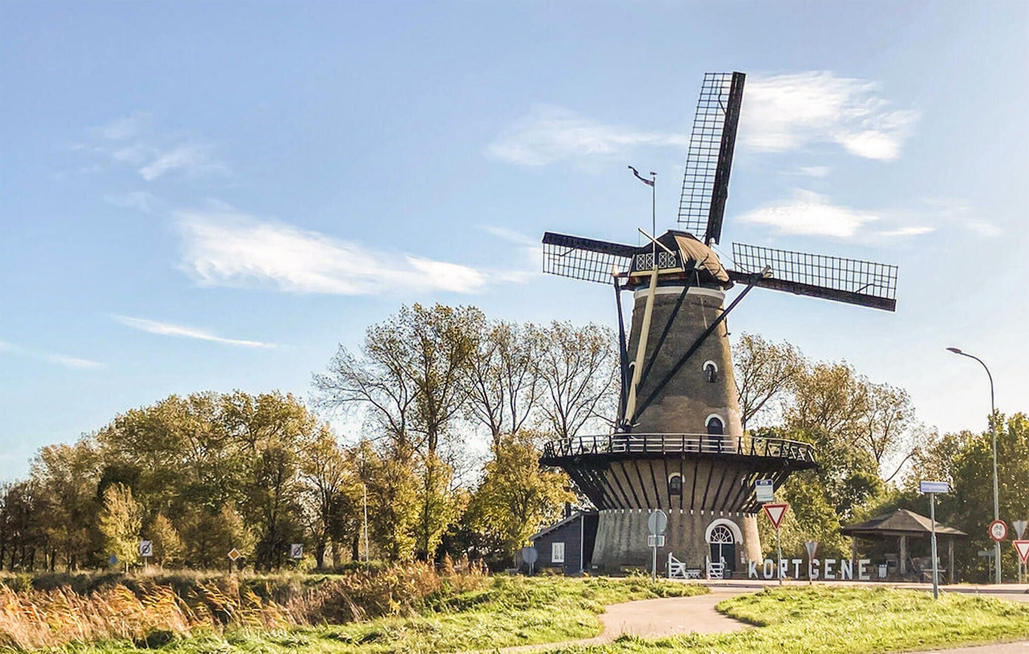 A traditional windmill with a tower and a rotating structure, surrounded by trees and a pathway.