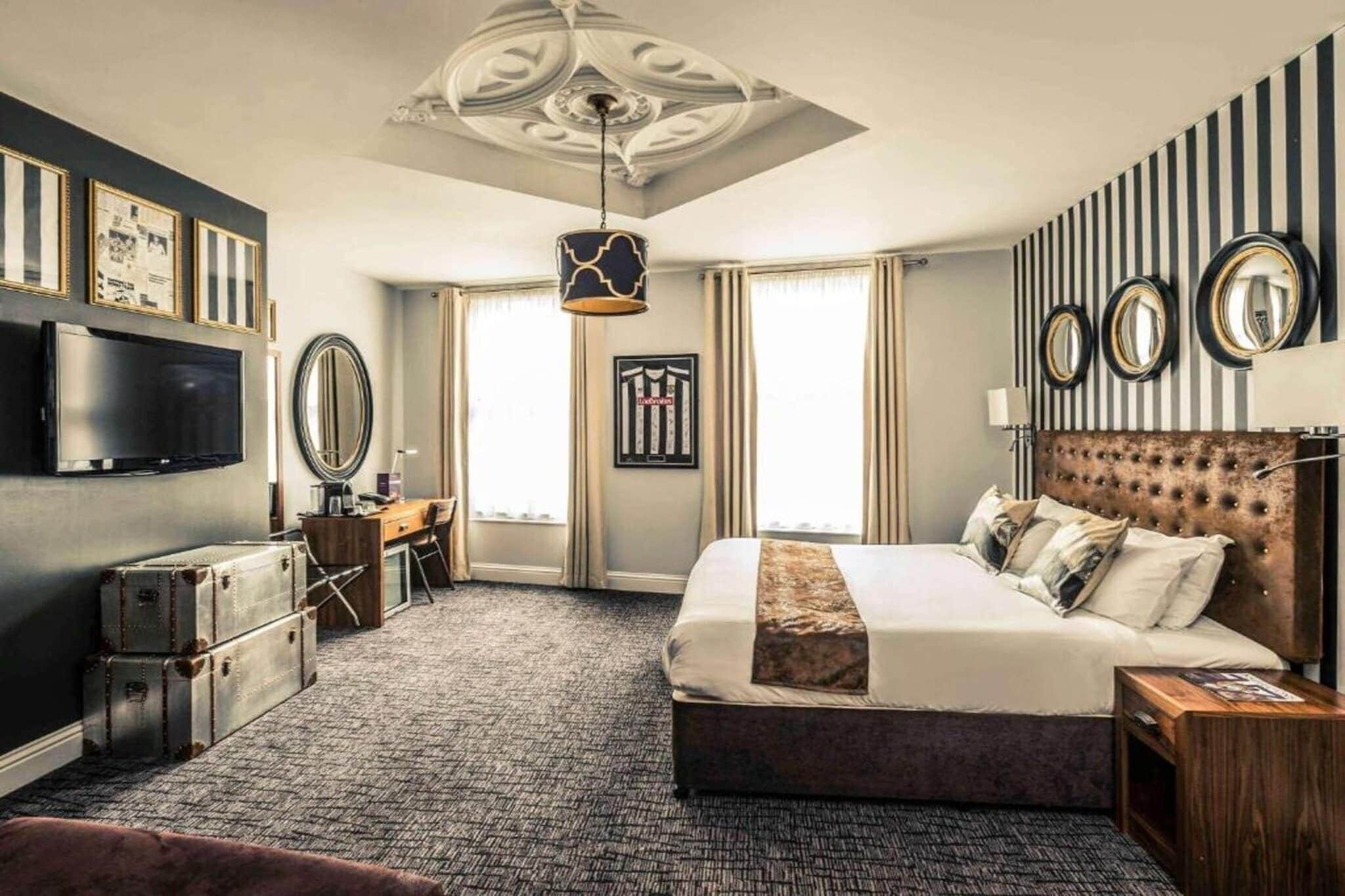 Una camera d'albergo con un letto grande, una scrivania, una televisione e un soffitto con decorazioni.