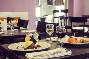 Une salle de restaurant avec des tables dressées pour le service, des verres à vin et des assiettes remplies de nourriture.