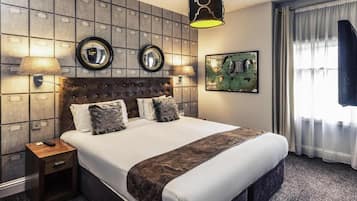 Une chambre d’hôtel avec un grand lit, deux lampes fixées au mur, un miroir et un tableau accroché au mur.