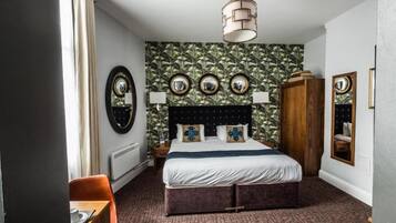 A hotel room with a bed, a wooden wardrobe, a mirror, and a dining area with a table and chairs.