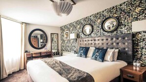 Ein Hotelzimmer mit einem großen Bett, zwei Nachttischen, einem Schreibtisch, einem Sessel und einem großen Spiegel an der Wand.
