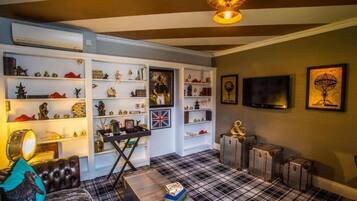 A room with a checkered floor, white shelving with various items, a black leather sofa, and a television mounted on the wall.