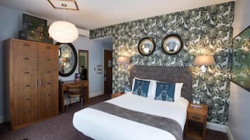 A bedroom with a large bed, two bedside lamps, a wooden wardrobe, a desk, and a mirror on the wall.