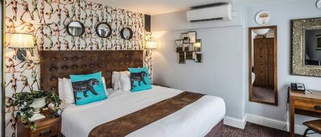 Habitación de hotel con una cama grande, cabecera de madera, mesita de noche con lámpara, escritorio con silla y espejo en la pared.