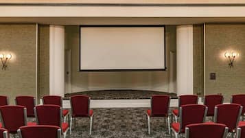 A conference room with a large screen, red chairs, carpeted floor, and wall sconces.