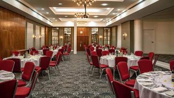 A banquet hall with round tables, red chairs, and a patterned carpet.