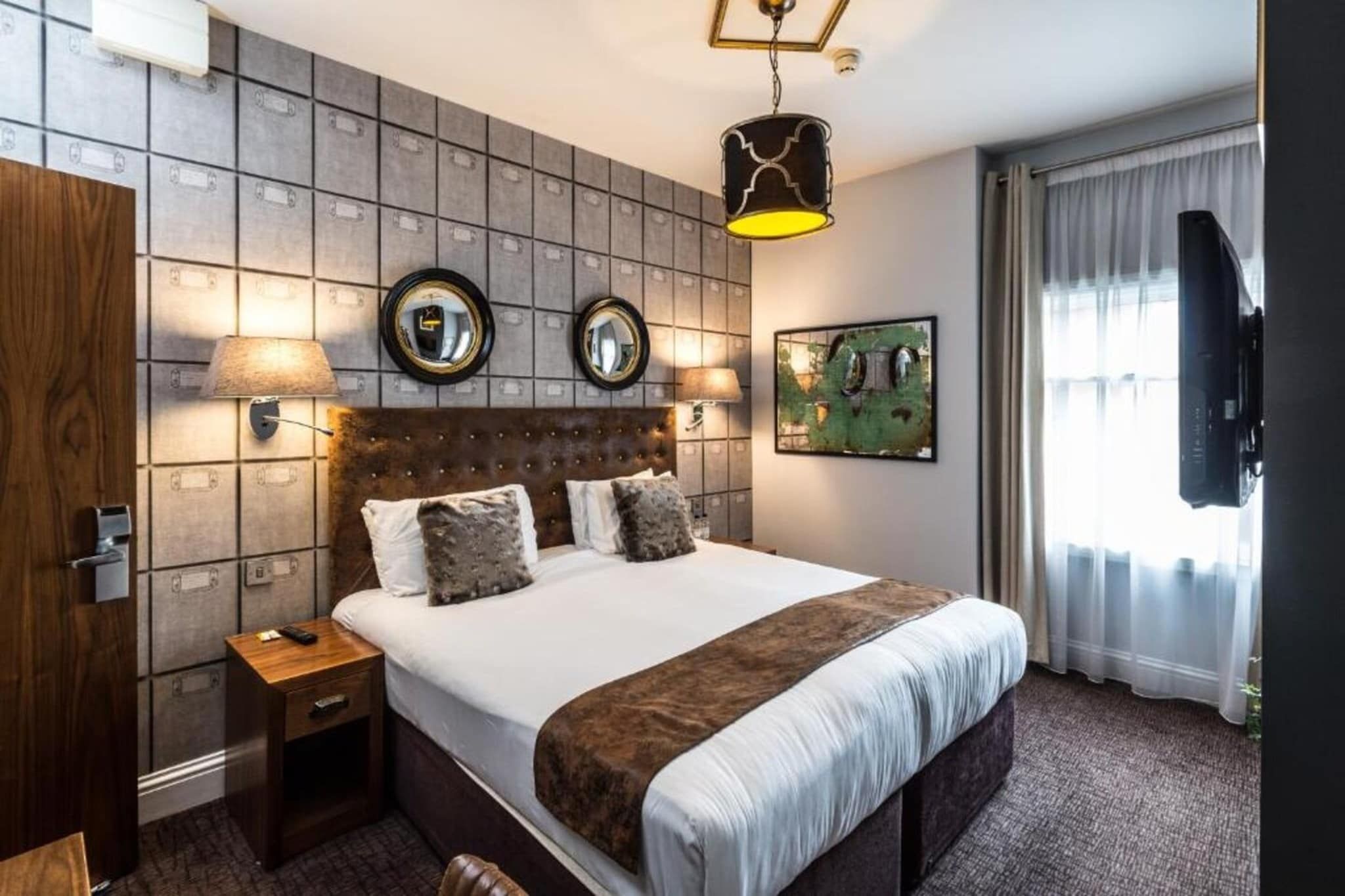 A hotel room with a large bed, two wall-mounted mirrors, a mounted television, and a window with curtains.
