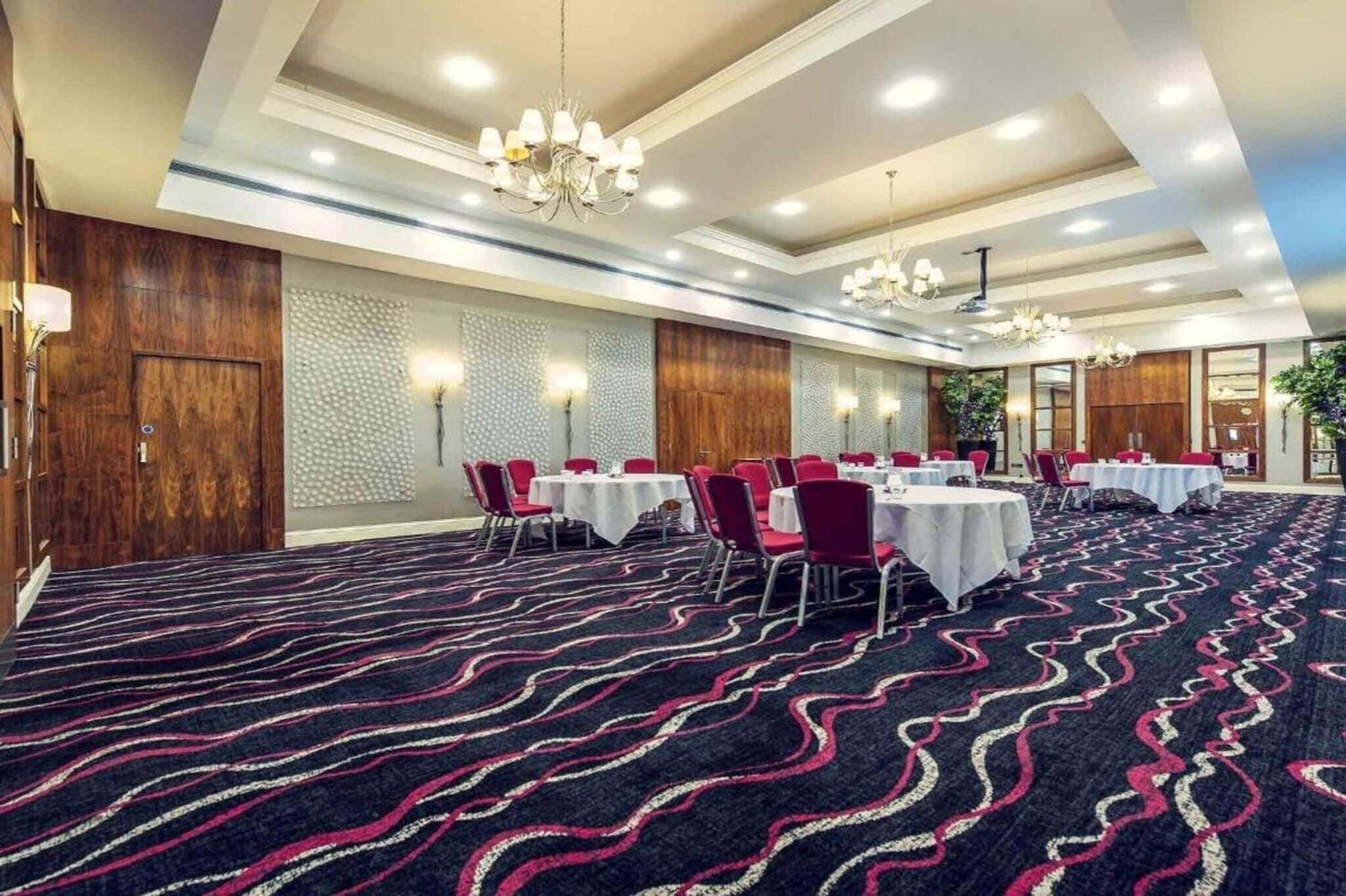 A conference room with round tables, red chairs, and a patterned carpet.