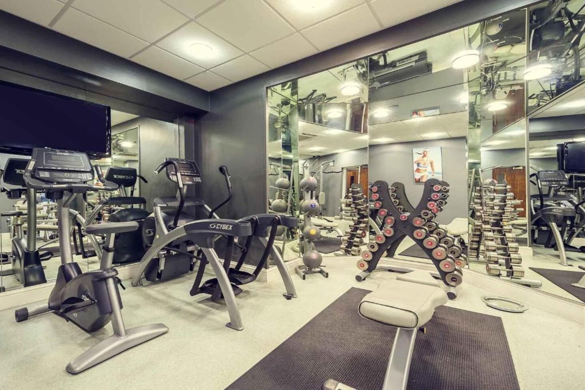 A gym with exercise equipment, mirrors, and a television.