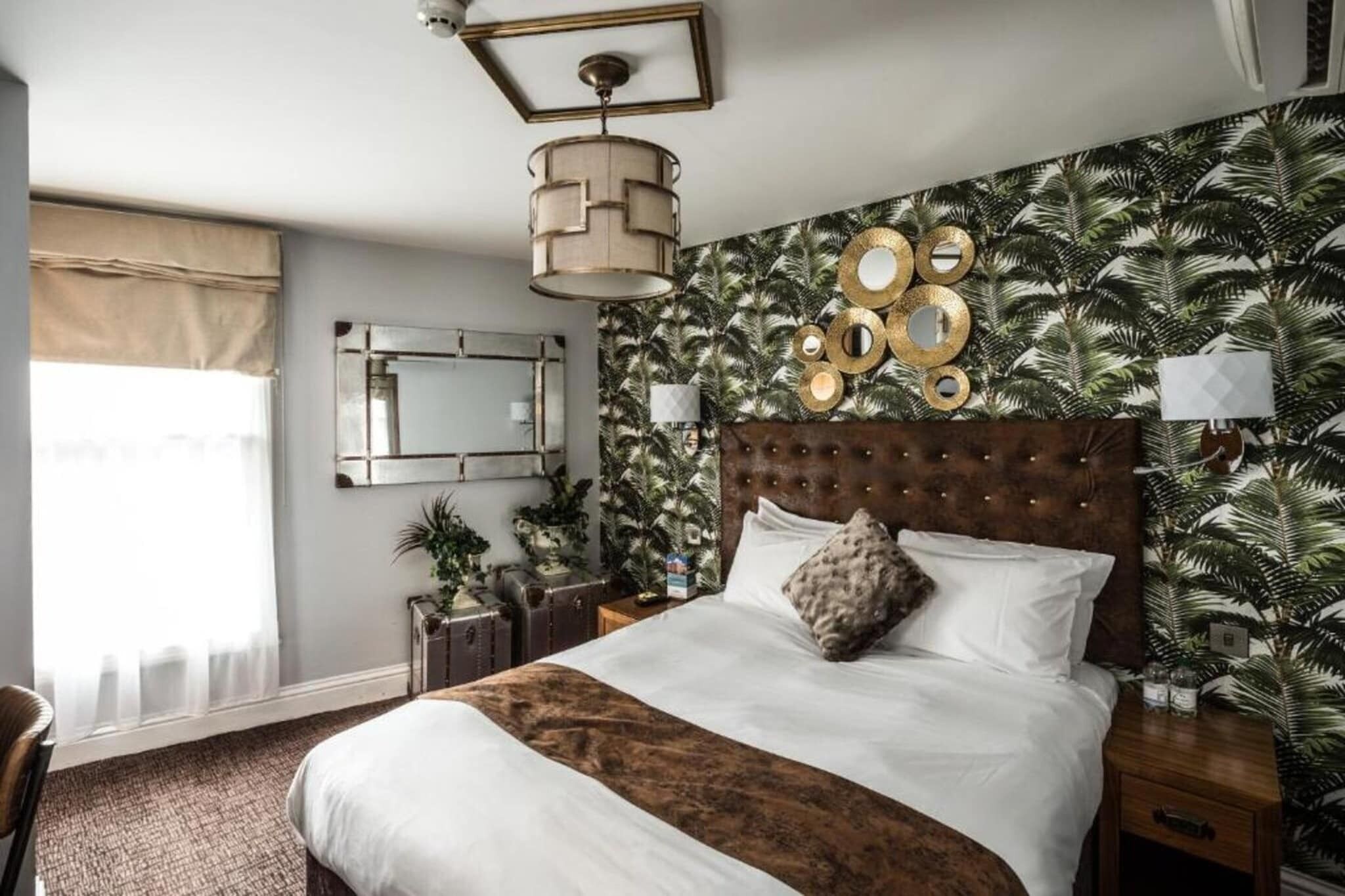 Een slaapkamer met een groot bed, een spiegel, een wandklok en tropisch behang.