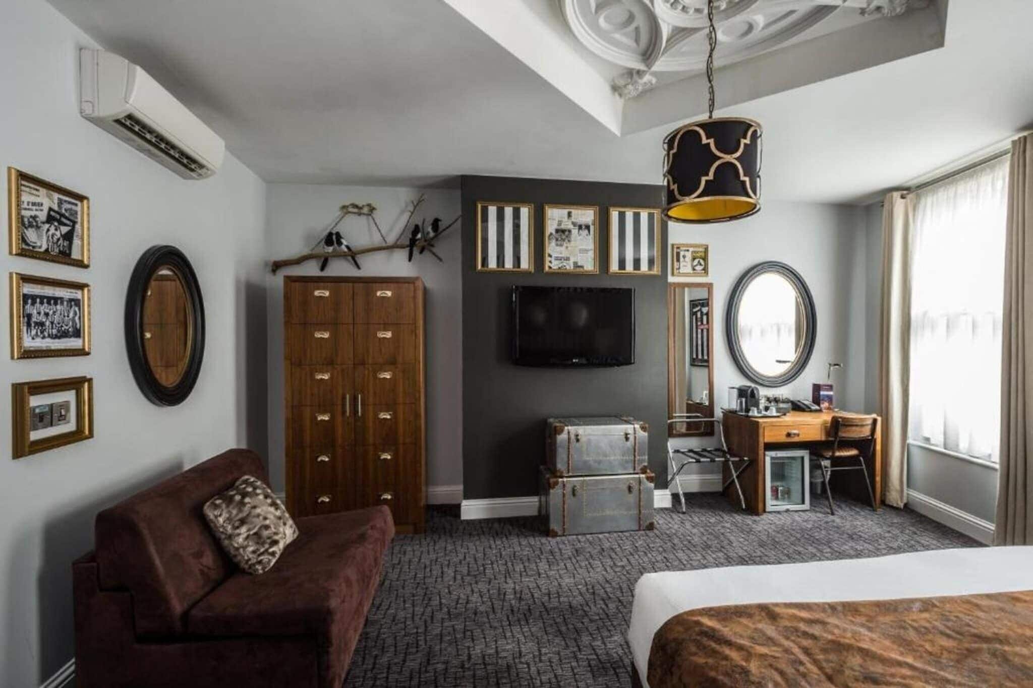 A hotel room with a bed, a sofa, a desk, a television, a wardrobe, and a mirror.