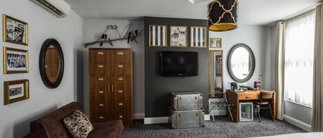 A hotel room with a bed, a sofa, a desk, a television, a wardrobe, and a mirror.