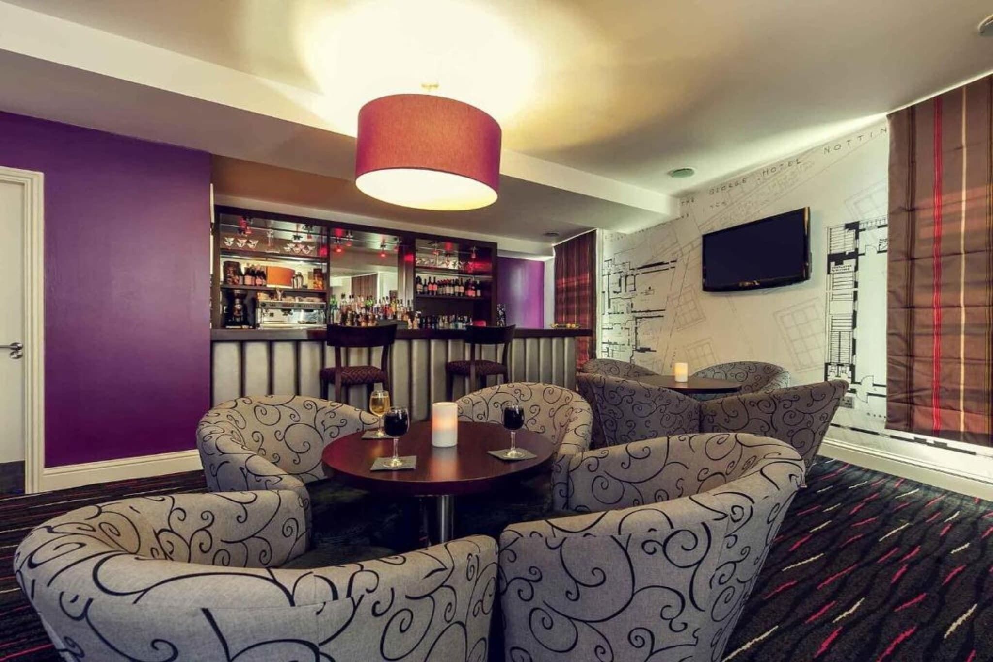A bar area with a purple wall, a television mounted on the wall, and a patterned sofa set.