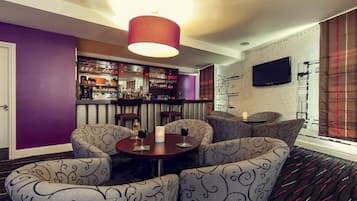 A bar area with a purple wall, a television mounted on the wall, and a patterned sofa set.