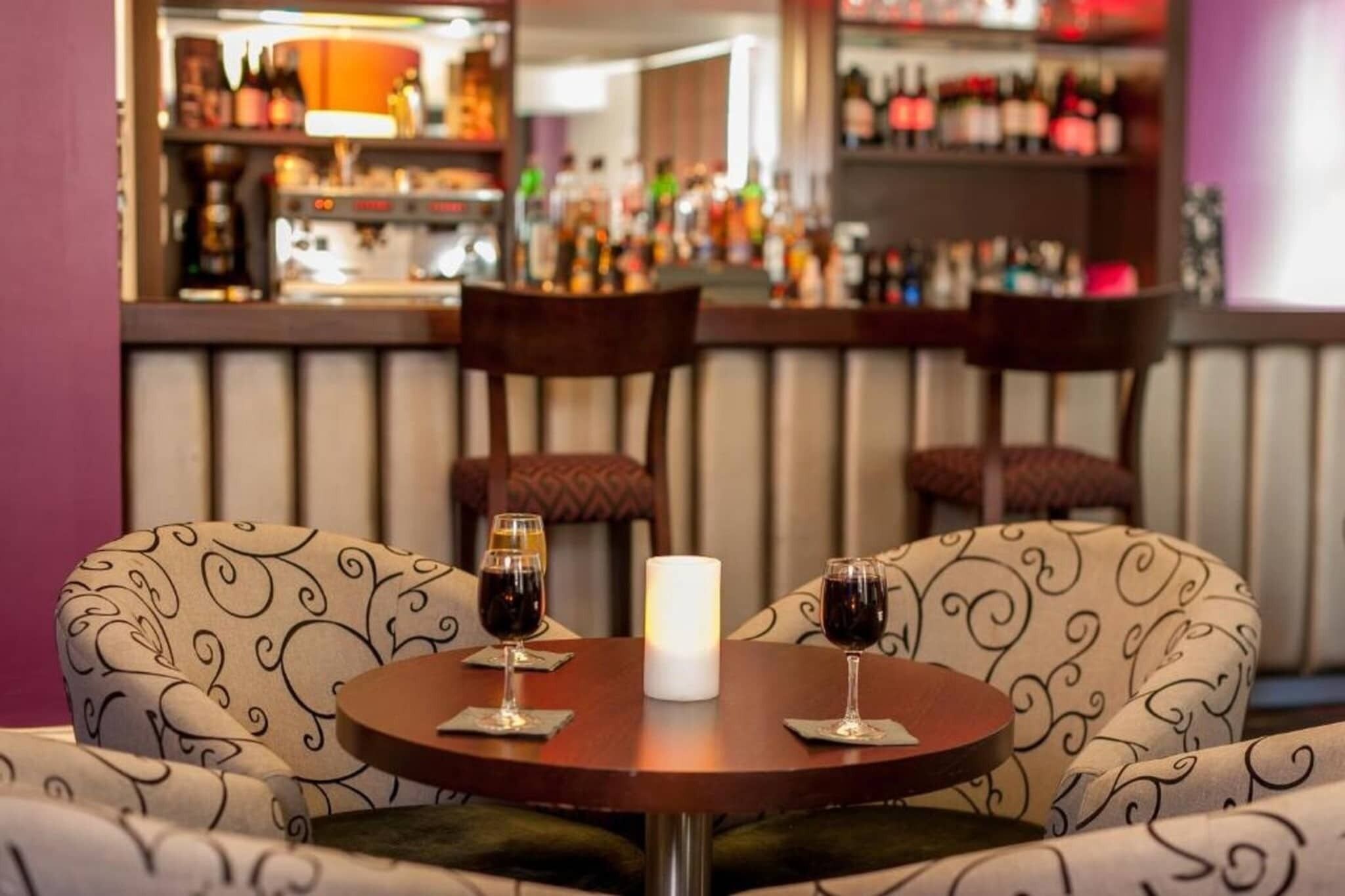 En bar med to runde borde, hver med et glas rødvin og et stearinlys.