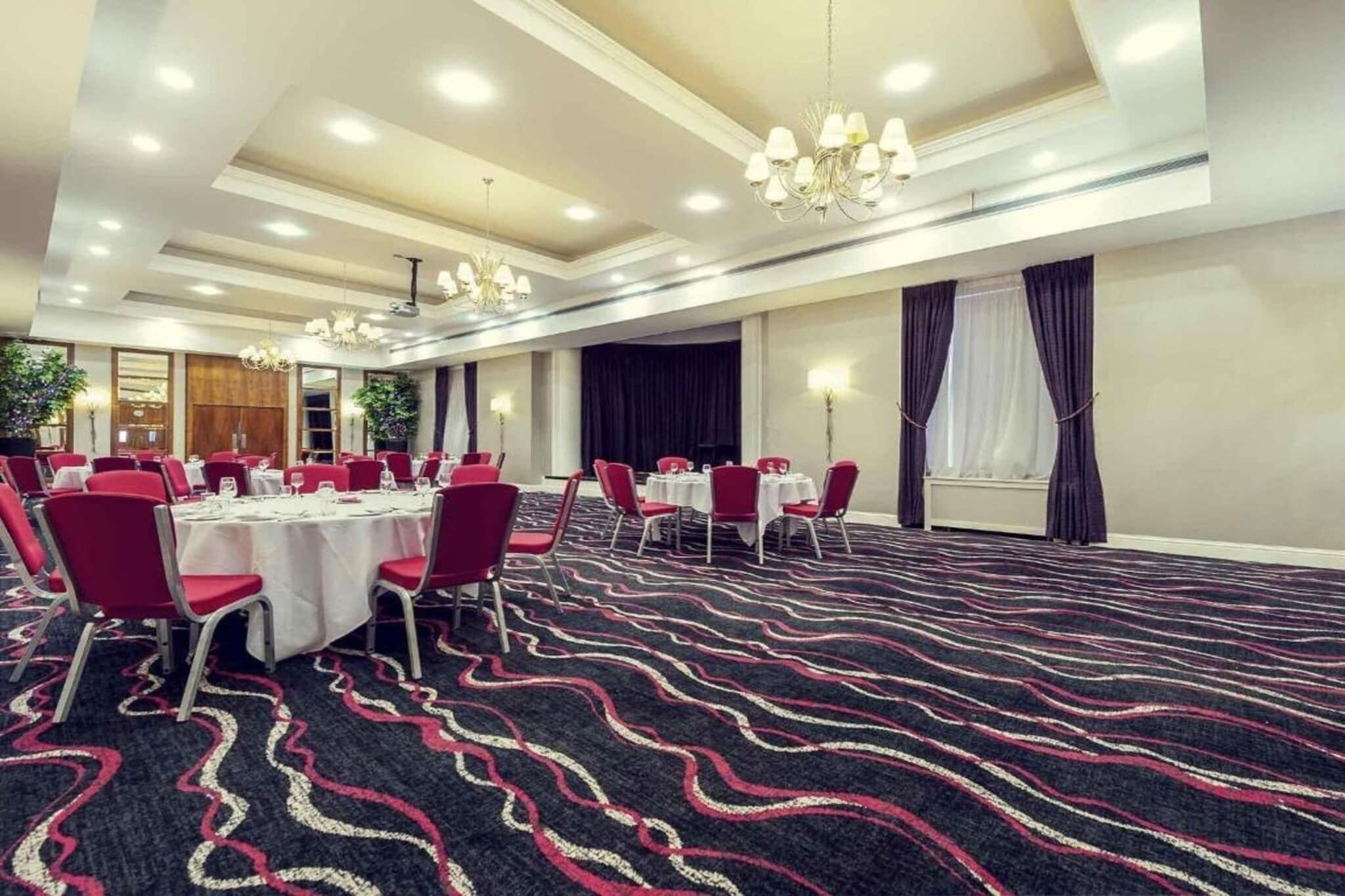 Una sala conferenze con tavoli rotondi, sedie rosse e una moquette fantasia.