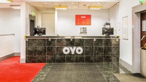 Een receptiebalie met 'OYO' branding, een digitaal scherm en een rode loper die naar de ingang leidt.