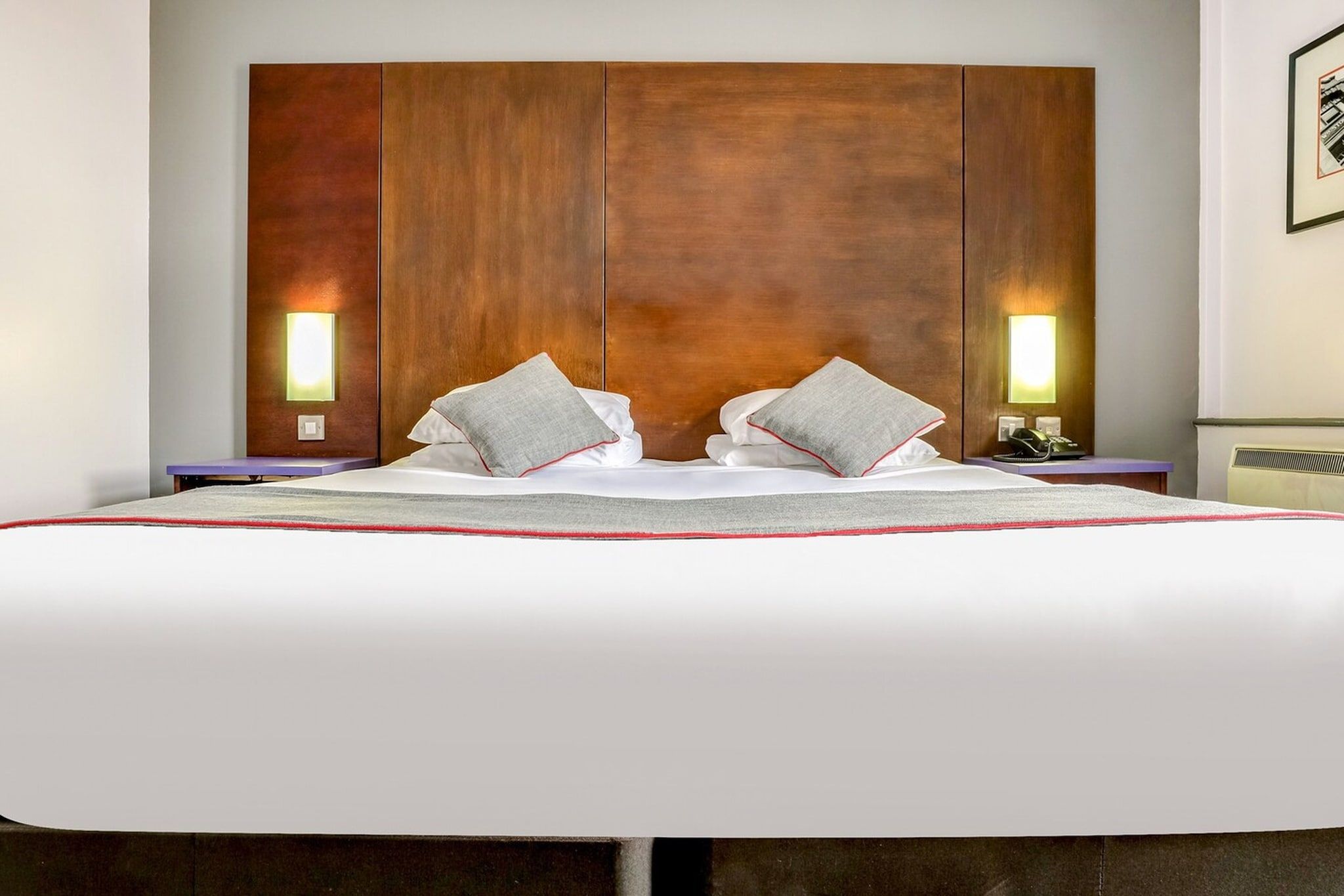 A double bed with a wooden headboard, two bedside lamps, and a red accent on the bedspread.