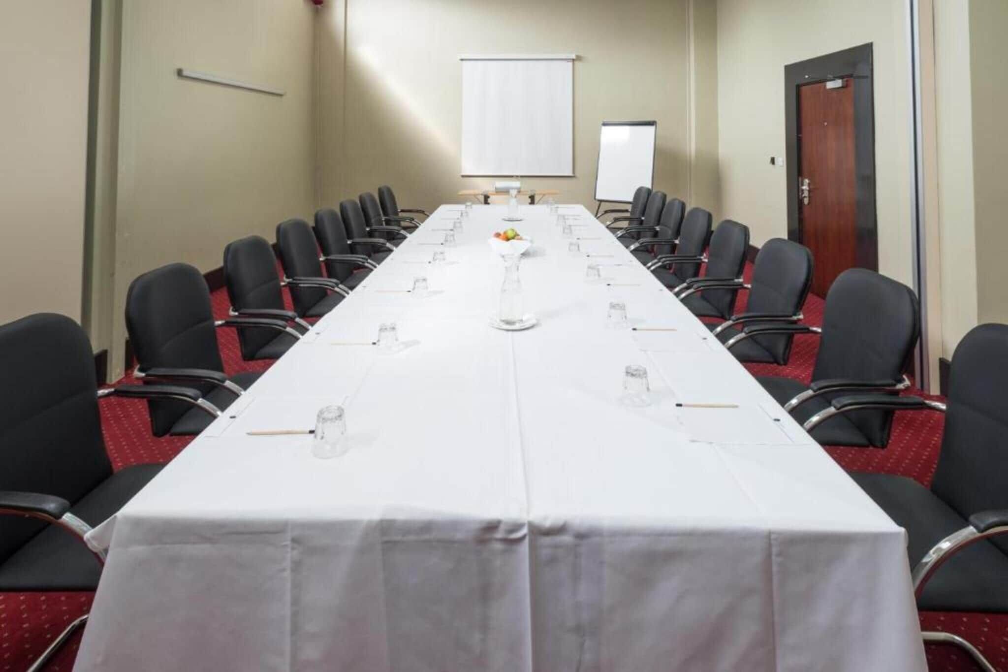 Un salón de conferencias con una larga mesa, sillas y una pizarra.