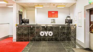 Vastaanottotiski, jossa on OYO-brändin logo, digitaalinen näyttö ja punainen matto, joka johtaa sisäänkäynnille.