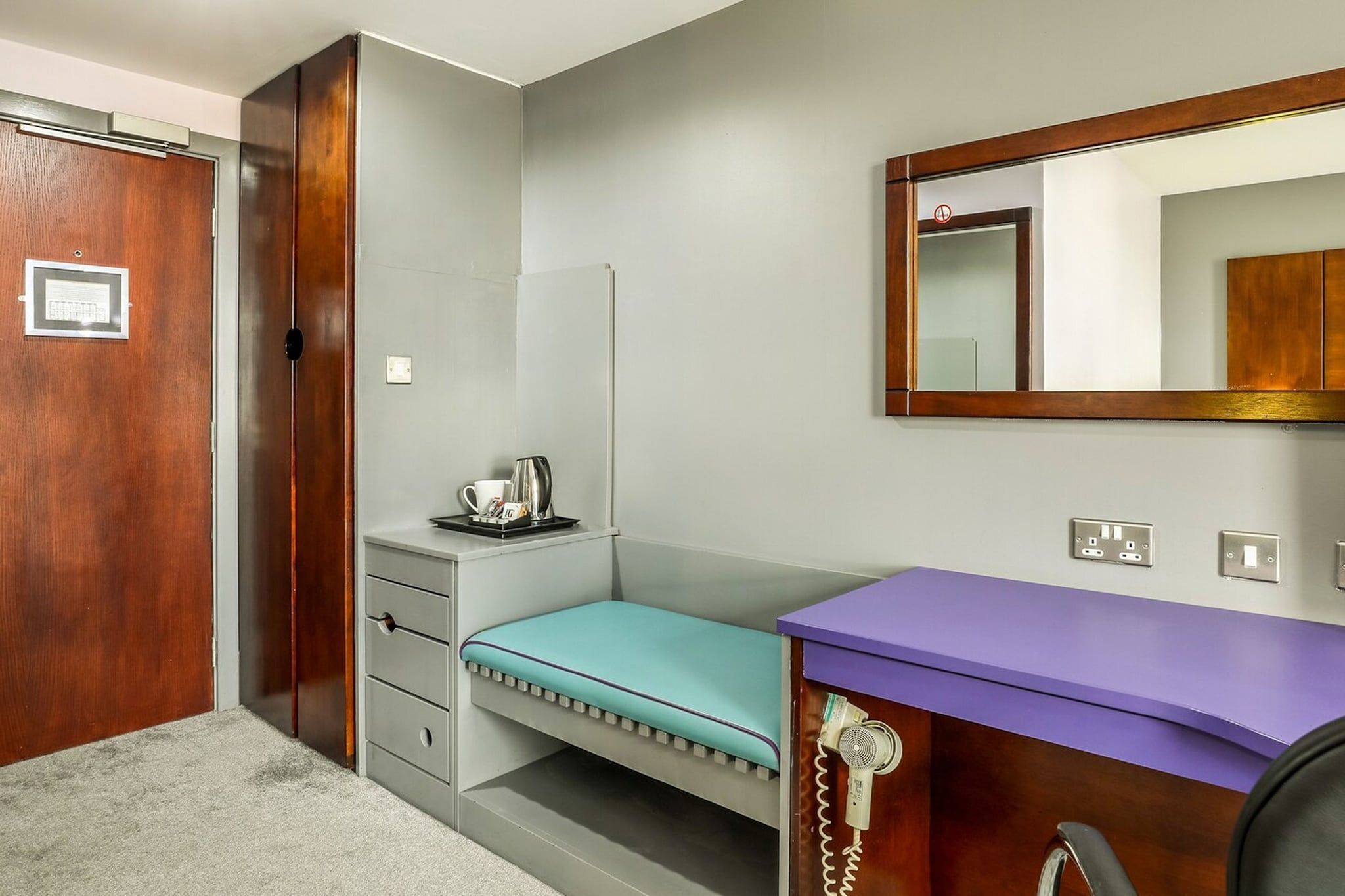 Une pièce avec une porte en bois, un petit banc, un comptoir violet, un téléphone et un miroir.