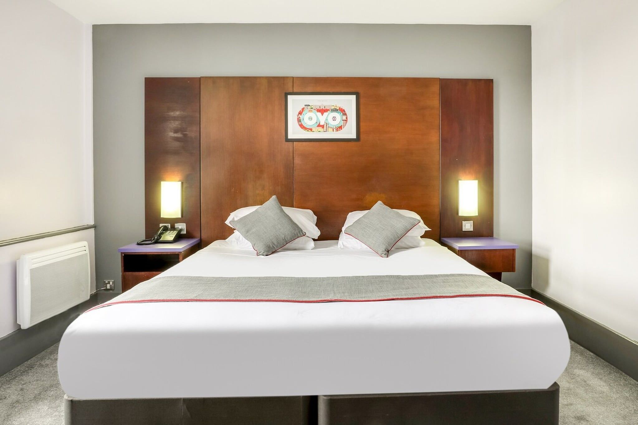 A hotel room with a large bed, two bedside tables with lamps, a framed picture on the headboard, and a telephone on one of the tables.