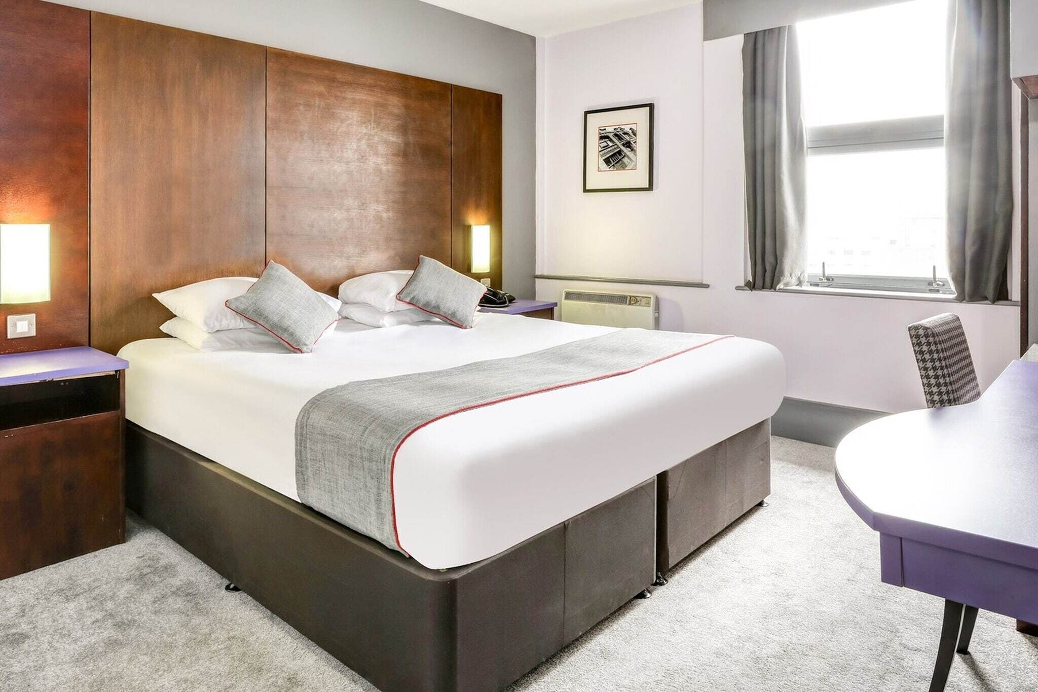 A hotel room with a large bed, bedside tables, a desk, and a window with curtains.