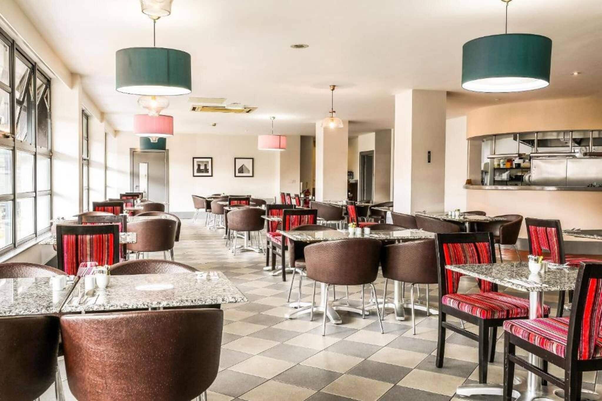 Un restaurant doté de nombreuses tables et chaises, de grandes fenêtres et de luminaires suspendus.