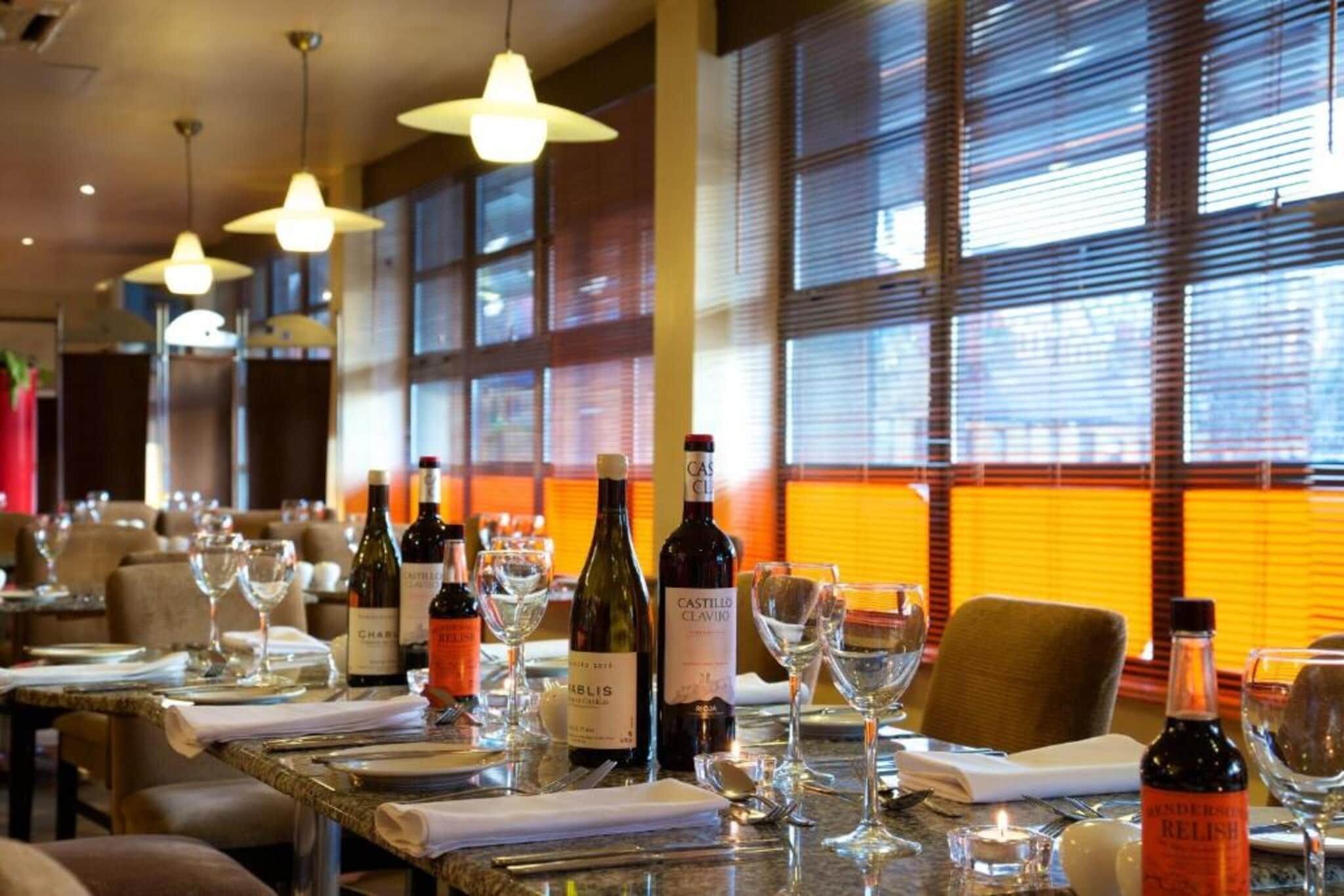 Interno di un ristorante con tavoli apparecchiati, bottiglie di vino e bicchieri.