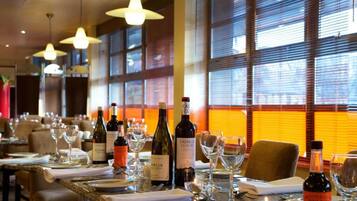 Interno di un ristorante con tavoli apparecchiati, bottiglie di vino e bicchieri.