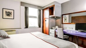 Habitación de hotel con cama, escritorio, silla, televisor y ventana con cortinas.