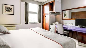 Une chambre d’hôtel équipée d’un lit, d’un bureau, d’une chaise, d’une télévision et d’une fenêtre avec des rideaux.