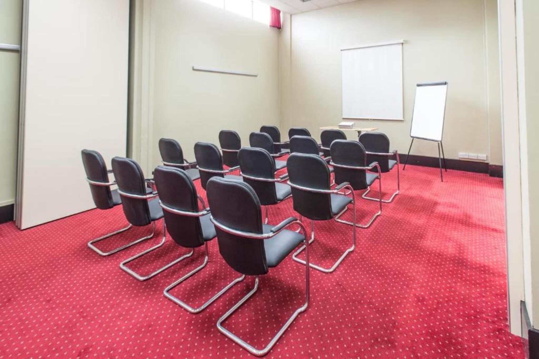 Un salón de conferencias con filas de sillas, una pizarra y un suelo cubierto de alfombra roja.