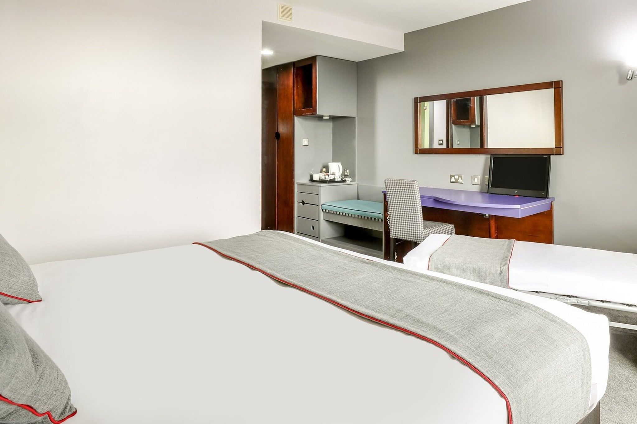 Une chambre d’hôtel équipée d’un lit, d’un bureau, d’une chaise, d’un miroir et d’une télévision.